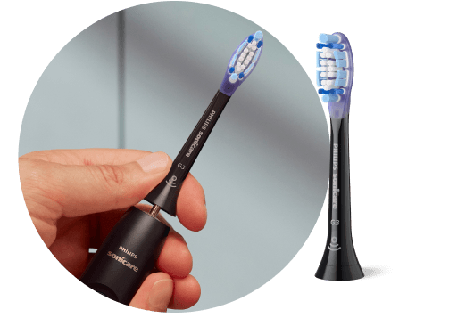 Dłoń trzymająca szczoteczkę z wyjętą końcówką. Obok znajduje się końcówka szczoteczki.