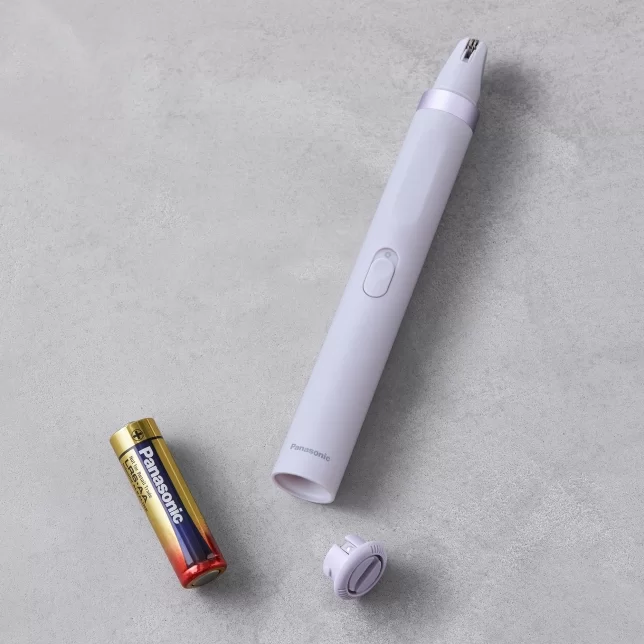Depilator do twarzy zasilany bateryjnie, leżący na blacie obok baterii Panasonic AA i nasadki