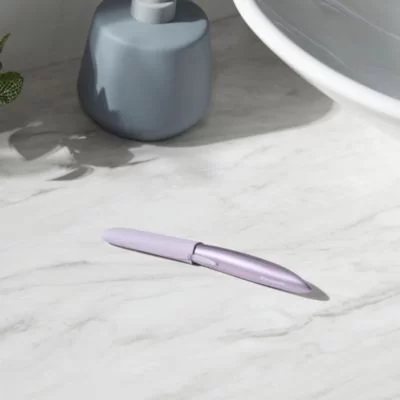 Elegancki, fioletowy trymer do twarzy z założoną nasadką, leżący na marmurowym blacie w łazience